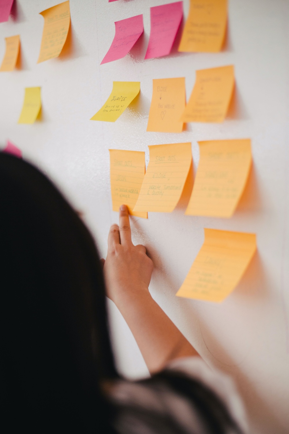 A person pointing at post-it notes on a Kanban board